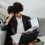 A woman working from home with a laptop and paperwork spread around her, reflecting the overlap of paid work, mental load, and invisible labour.