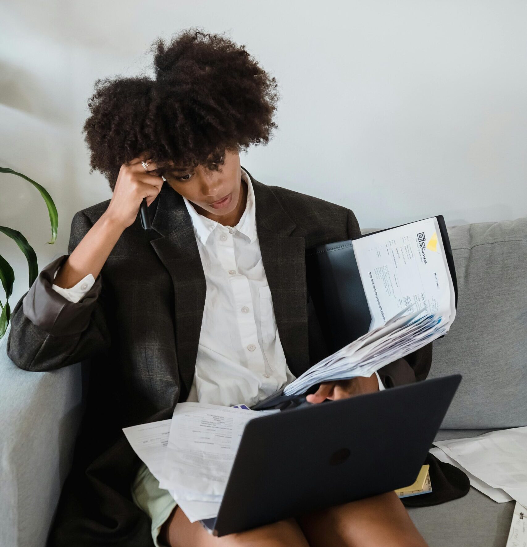 A woman working from home with a laptop and paperwork spread around her, reflecting the overlap of paid work, mental load, and invisible labour.