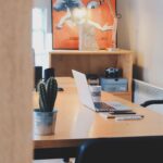 A modern office desk setup featuring a cactus plant, laptop, and stylish decor in a contemporary office space.